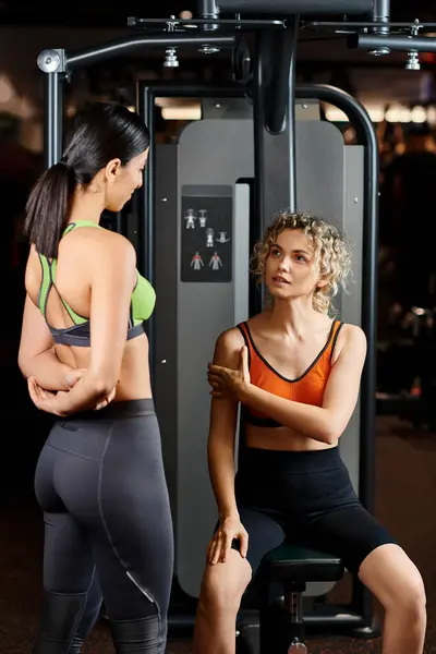 Cheerful female coach explaining to her appealing jolly client how to use chest press machine — Stock Photo