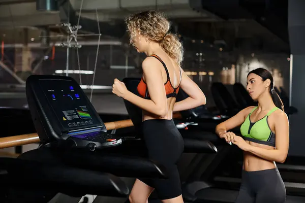 Good looking athletic female coach and her blonde client in sportwear exercising on treadmill in gym — Stock Photo