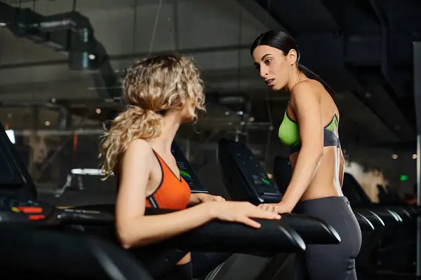Добре виглядає енергійний жіночий тренер і блондинка-клієнт в спортивному одязі вправи на біговій доріжці в спортзалі — стокове фото