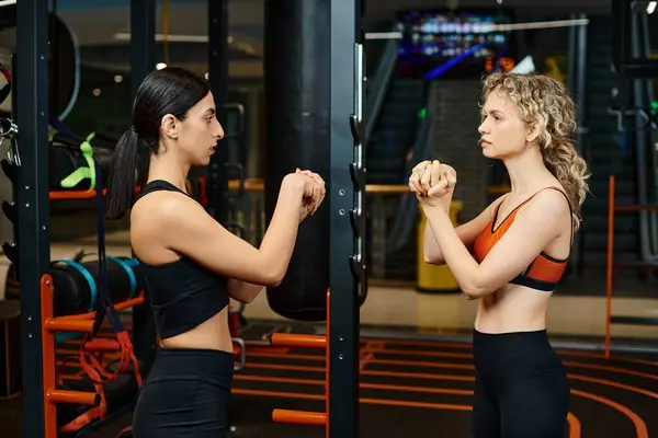 Atractiva entrenadora femenina ayudando a su cliente atractivo rubia a estirar sus músculos mientras está en el gimnasio - foto de stock