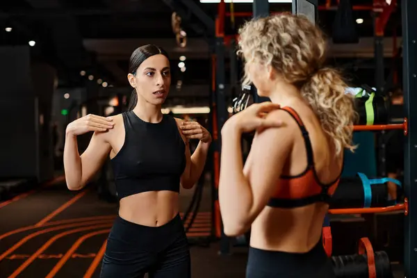 Atlética atractiva entrenadora femenina en ropa deportiva ayudando a su hermoso cliente a estirar sus músculos - foto de stock