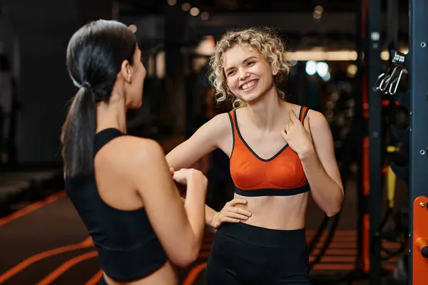 Спортивний весела жінка-тренер допомагає їй блондинка веселий клієнт, щоб розтягнути її м'язи під час тренажерного залу — стокове фото