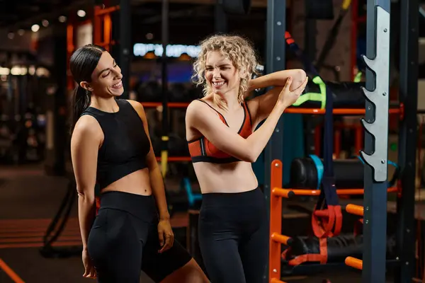 Energische, fröhliche Trainerin, die ihrem blonden fröhlichen Kunden hilft, ihre Muskeln im Fitnessstudio zu dehnen — Stockfoto