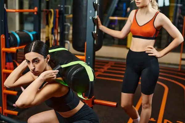 Attractive sporty woman and her athletic female coach practicing with power bag while in gym — Stock Photo