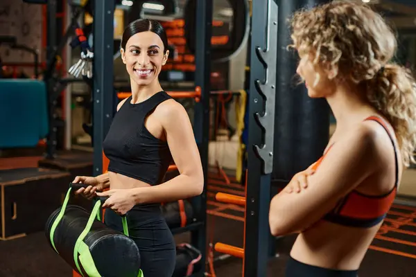 Alegre mujer guapa y su entrenador atlético femenino practicando con bolsa de poder mientras está en el gimnasio - foto de stock