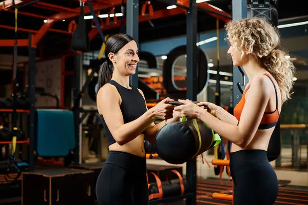 Joyeux belle femme et son entraîneur féminin athlétique pratiquant avec sac de puissance tandis que dans la salle de gym — Photo de stock