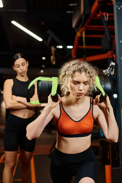 Focus on blonde attractive woman exercising with power bag with her blurred female coach on backdrop — Stock Photo