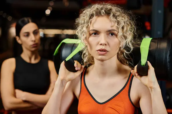 Focus on blonde attractive woman exercising with power bag with her blurred female coach on backdrop — Stock Photo