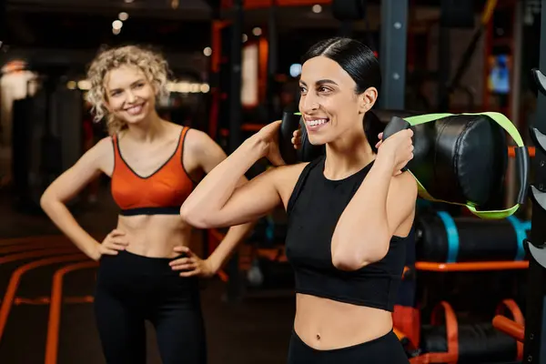 Alegre atractiva mujer y su entrenador atlético mujer practicando con bolsa de poder mientras que en el gimnasio - foto de stock