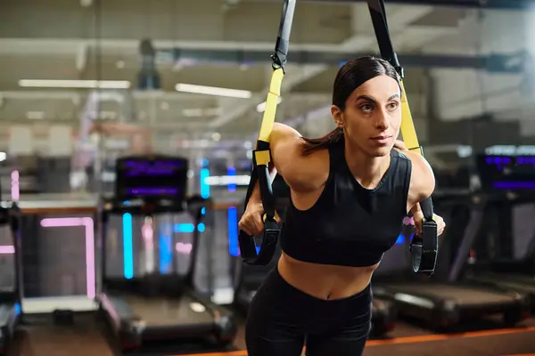 Atraente mulher esportiva com cabelo morena em roupas esportivas confortáveis usando equipamentos pull-ups no ginásio — Fotografia de Stock