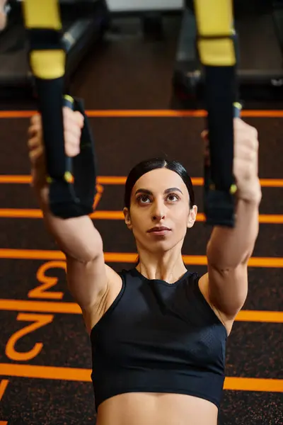 Привлекательная спортивная женщина с брюнетками в удобной спортивной форме с помощью подтягивающего оборудования в тренажерном зале — стоковое фото