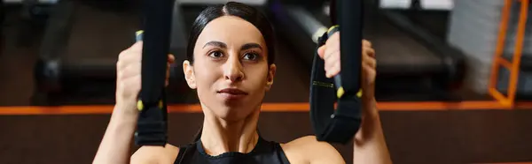 Mulher enérgica com cabelo morena em roupas esportivas confortáveis usando equipamentos pull ups no ginásio, banner — Fotografia de Stock