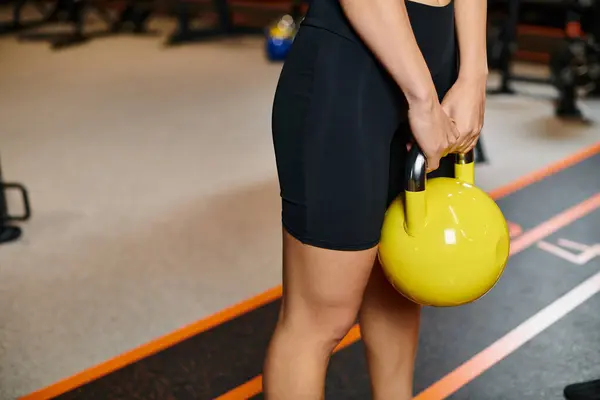 Cropped view of athletic active woman in cozy black sportwear exercising with yellow kettlebell — Stock Photo