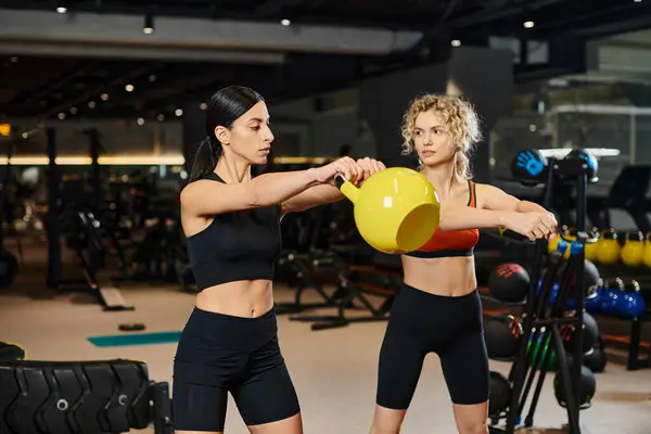 Vigorous attractive coach in comfy sportwear watching her client using kettlebell while in gym — Stock Photo