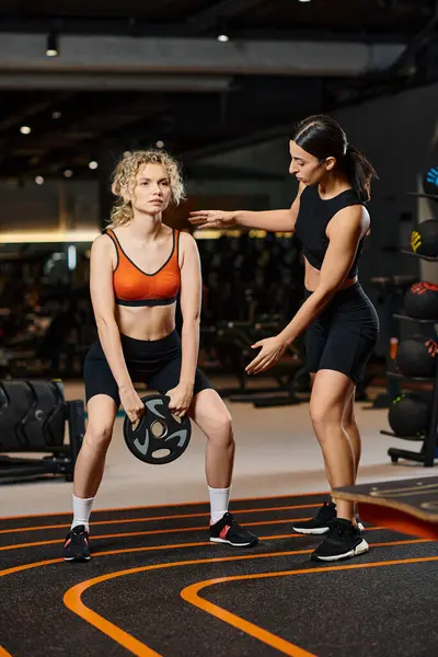 Attractive athletic female coach in black sportwear explaining how to use weight plate to her client — Stock Photo