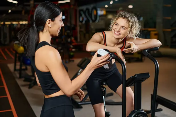 Beautiful energetic woman using modern cross trainer while in gym next to her athletic female coach — Stock Photo