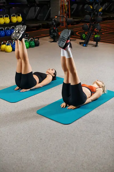 Attractive vigorous female coach and her client in sportwear warming up on fitness mats while in gym — Stock Photo