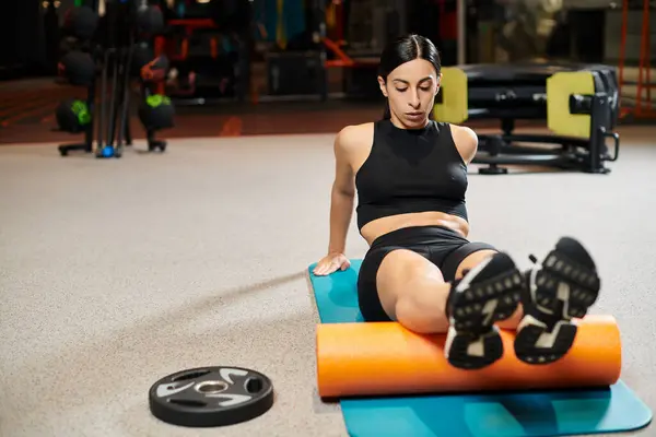 Mulher bonita com cabelo escuro em confortável sportwear preto praticando no tapete de fitness, enquanto no ginásio — Fotografia de Stock