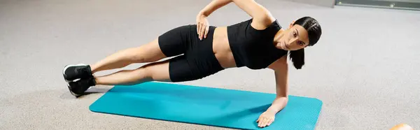 Bella donna con i capelli scuri in abbigliamento sportivo che si estende attivamente sul tappeto fitness mentre in palestra, banner — Foto stock