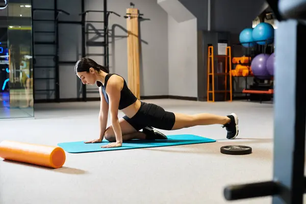 Appealing woman with dark hair in black sportwear stretching actively on fitness mat while in gym — Stock Photo