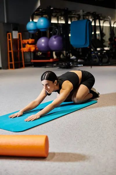 Good looking woman with dark hair in black sportwear stretching actively on fitness mat while in gym — Stock Photo