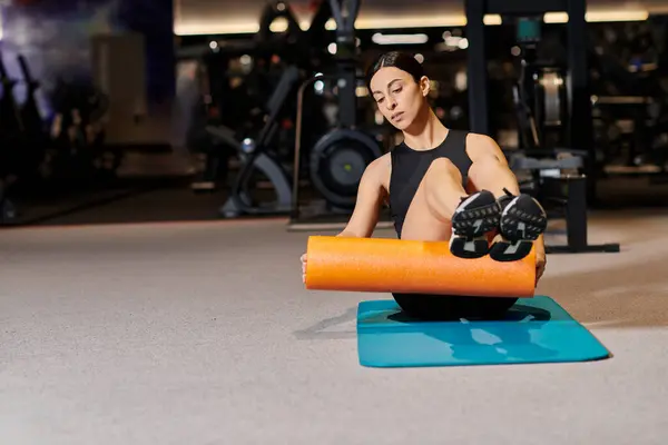 Appealing energetic woman in black sportwear practicing on fitness mat with roller while in gym — Stock Photo