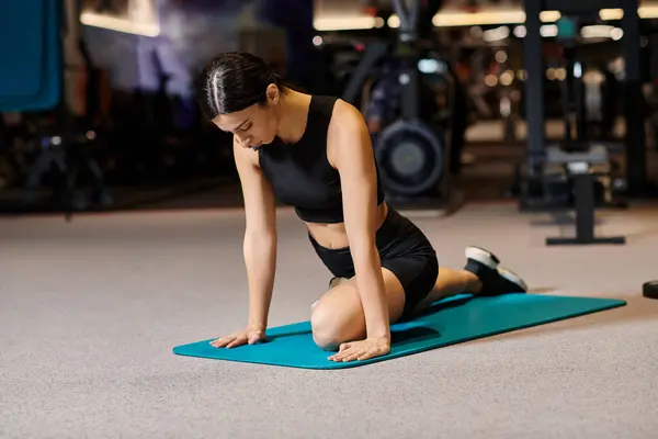 Bella donna atletica con i capelli scuri che allunga i muscoli sul tappeto fitness mentre in palestra — Foto stock