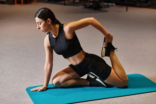 Приваблива спортсменка в чорному спортивному одязі розтягує м'язи на фітнес-маті під час занять спортом — стокове фото