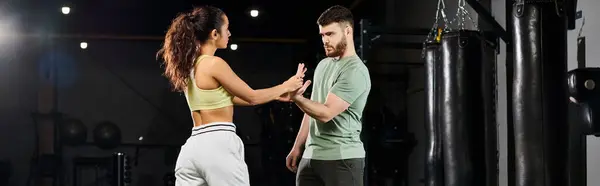 Entrenador de fitness masculino mostrando técnicas de autodefensa a una mujer en un gimnasio, enfocado y comprometido. - foto de stock