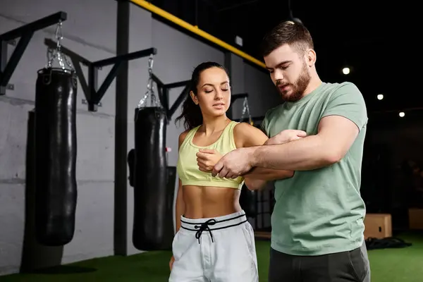 Un entrenador masculino instruye a una mujer en técnicas de autodefensa, de pie juntos en un gimnasio. - foto de stock