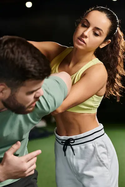 Un hombre, un entrenador de autodefensa, sostiene a una mujer en un abrazo protector mientras demuestra técnicas en un entorno de gimnasio. - foto de stock