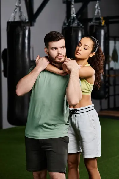 Un entrenador masculino demuestra técnicas de autodefensa a una mujer en un gimnasio, fomentando el empoderamiento y la unidad. - foto de stock