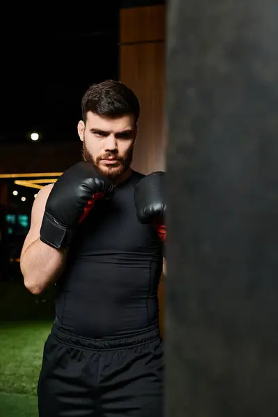 Красивий чоловік з бородою в боксерських рукавичках стоїть біля ударної сумки в спортзалі, готується до тренування. — стокове фото