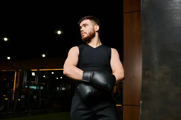 Hombre guapo con barba usando guantes de boxeo, lanzando potentes golpes a un saco de boxeo en un gimnasio. - foto de stock