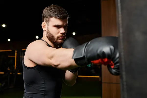 Un hombre guapo con barba usando guantes de boxeo, lanzando puñetazos a un saco de boxeo en un gimnasio. - foto de stock