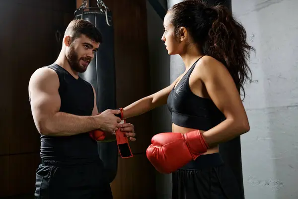 Um treinador masculino fica ao lado de uma esportista morena em uso ativo enquanto ela usa luvas de boxe e pratica em um ginásio. — Fotografia de Stock