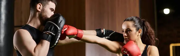 Um treinador masculino guia uma esportista morena no desgaste ativo enquanto eles se envolvem em uma sessão de boxe em um ginásio. — Fotografia de Stock