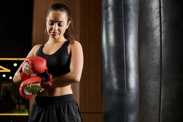 A brunette sportswoman in black active wear throwing punches with red boxing gloves at a gym. — Stock Photo