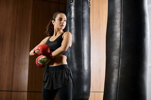A brunette sportswoman in active wear throws punches with red boxing gloves in a gym setting. — Stock Photo