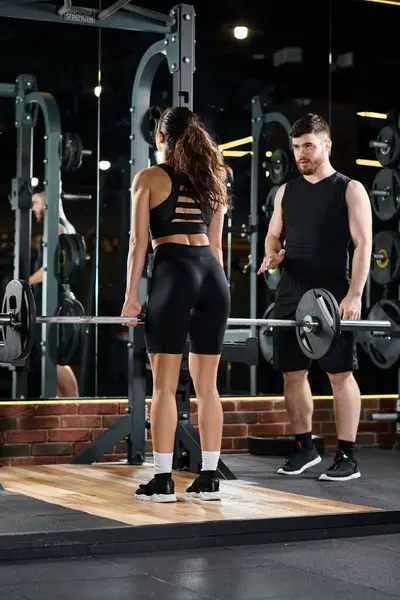 A male personal trainer assisting a brunette sportswoman in a gym with workout routines and equipment. — Stock Photo