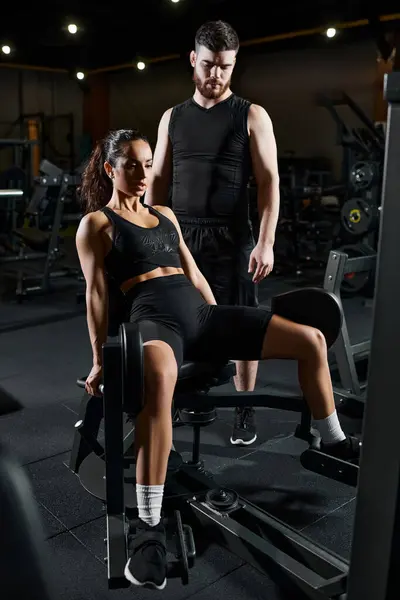 Una entrenadora personal se para con confianza junto a una decidida deportista morena en un gimnasio, motivándola y guiándola. - foto de stock