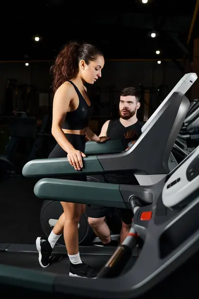 Um personal trainer masculino e uma esportista morena estão correndo energeticamente em uma esteira em um ginásio. — Fotografia de Stock