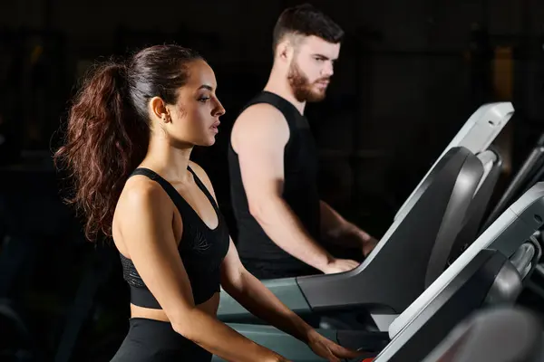 A male trainer and a brunette sportswoman are exerting themselves while running on a treadmill in a gym. — Stock Photo