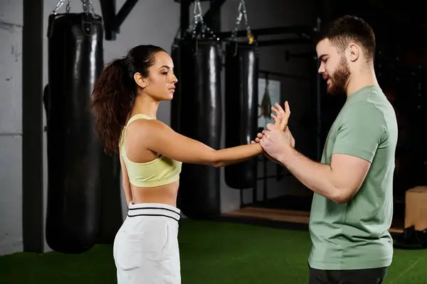 Un entraîneur masculin démontre des techniques d'auto-défense à une femme dans une salle de gym, mettant en valeur l'autonomisation et le travail d'équipe. — Photo de stock