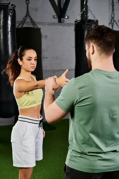 A male trainer guides a woman in learning self-defense techniques in a gym setting with focus and determination. — Stock Photo