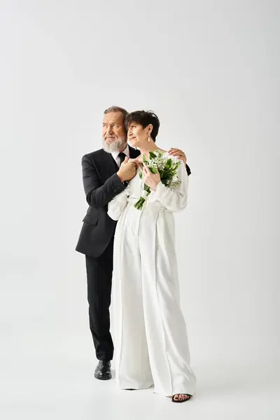 Noiva de meia-idade e noivo em traje de casamento posar apaixonadamente, irradiando alegria e amor em um estúdio. — Fotografia de Stock