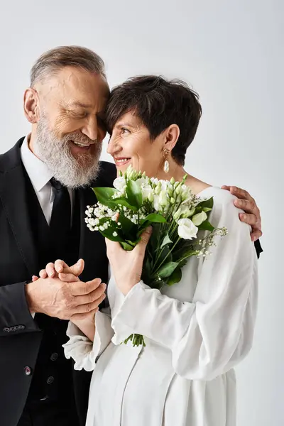 Una sposa e uno sposo di mezza età in abiti da sposa stanno fianco a fianco, celebrando il loro giorno speciale in un ambiente di studio. — Foto stock