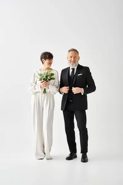 Middle-aged bride and groom in formal attire stand together in a studio, celebrating their special day with love and elegance. — Stock Photo