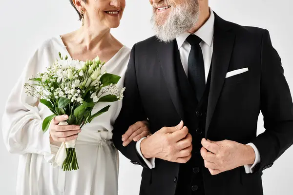 Un hombre de mediana edad en un esmoquin está junto a una mujer en un vestido blanco, exudando elegancia y sofisticación en un entorno de estudio. - foto de stock