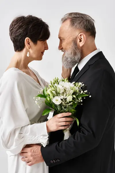 Mariée d'âge moyen et marié en robes de mariée se tiennent côte à côte, célébrant leur journée spéciale dans un cadre de studio. — Photo de stock